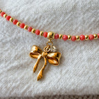 Detailaufnahme der Colette Schleifenkette mit vergoldeter Schleife und korallfarbenen Glasperlen