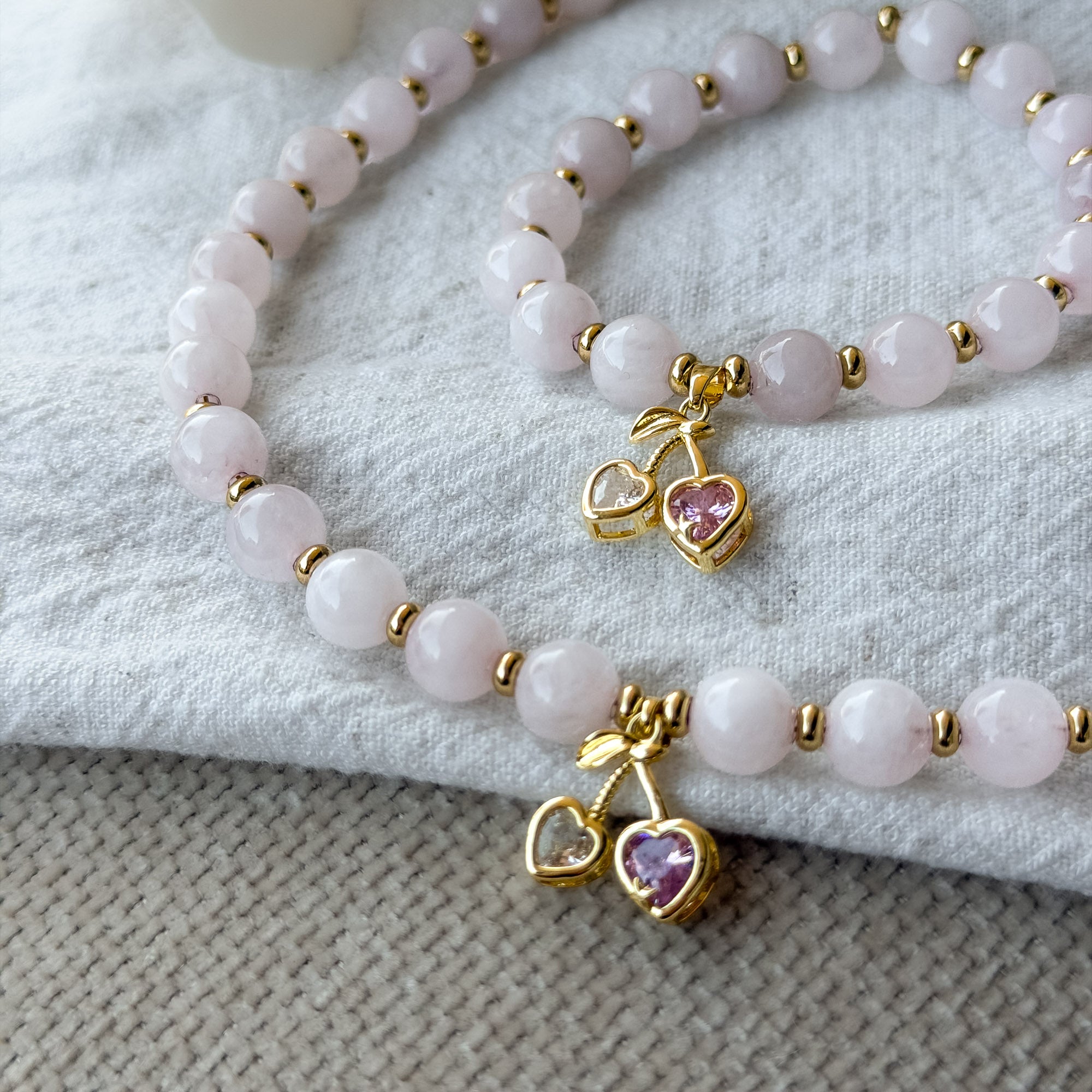 Detailaufnahme des Cherry Love Rosenquarz-Armbands aus natürlichen Rosenquarz-Perlen mit vergoldeten Zwischenperlen und Kirsch-Anhänger, passend zur Cherry Love Rosenquarz-Kette