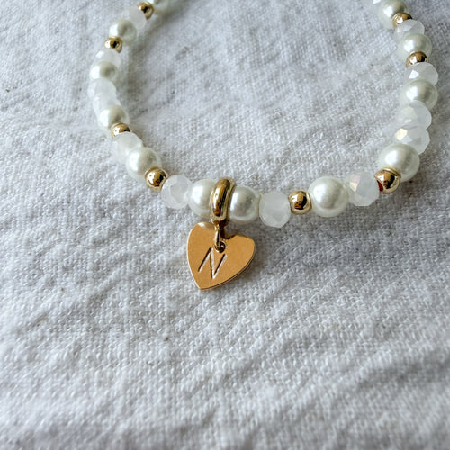 Personalisiertes Perlenarmband mit graviertem Herz-Anhänger, weißen Muschelperlen, weißen Glasperlen und vergoldeten Details.